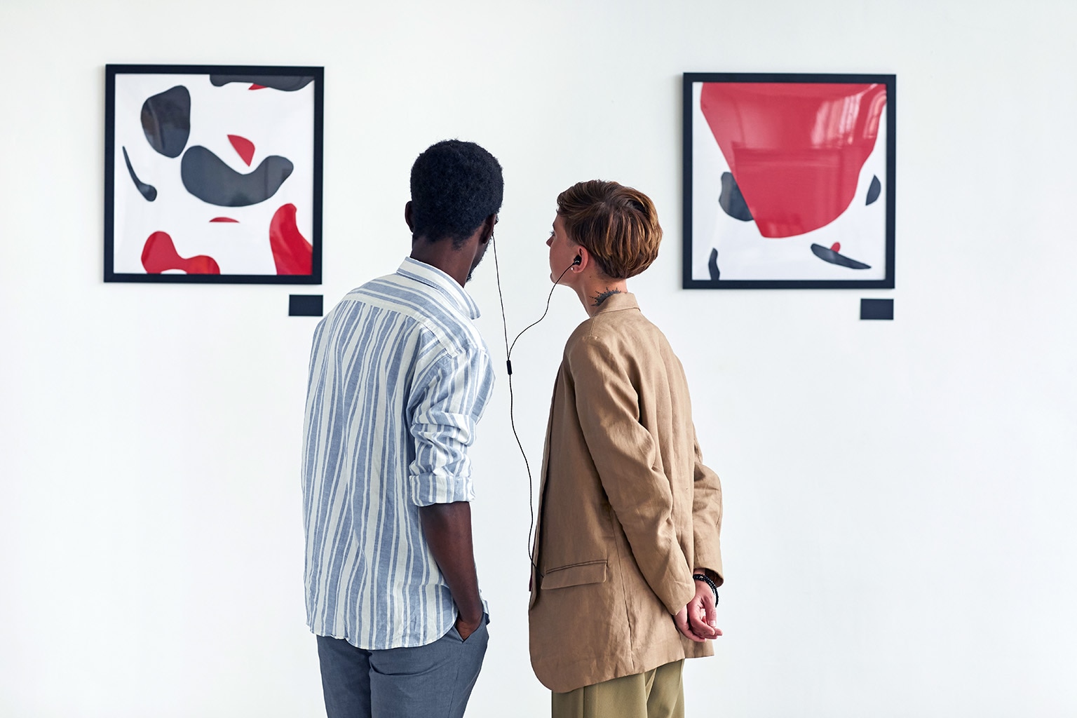 Two people sharing a set of ear buds while looking at modern art in a museum.