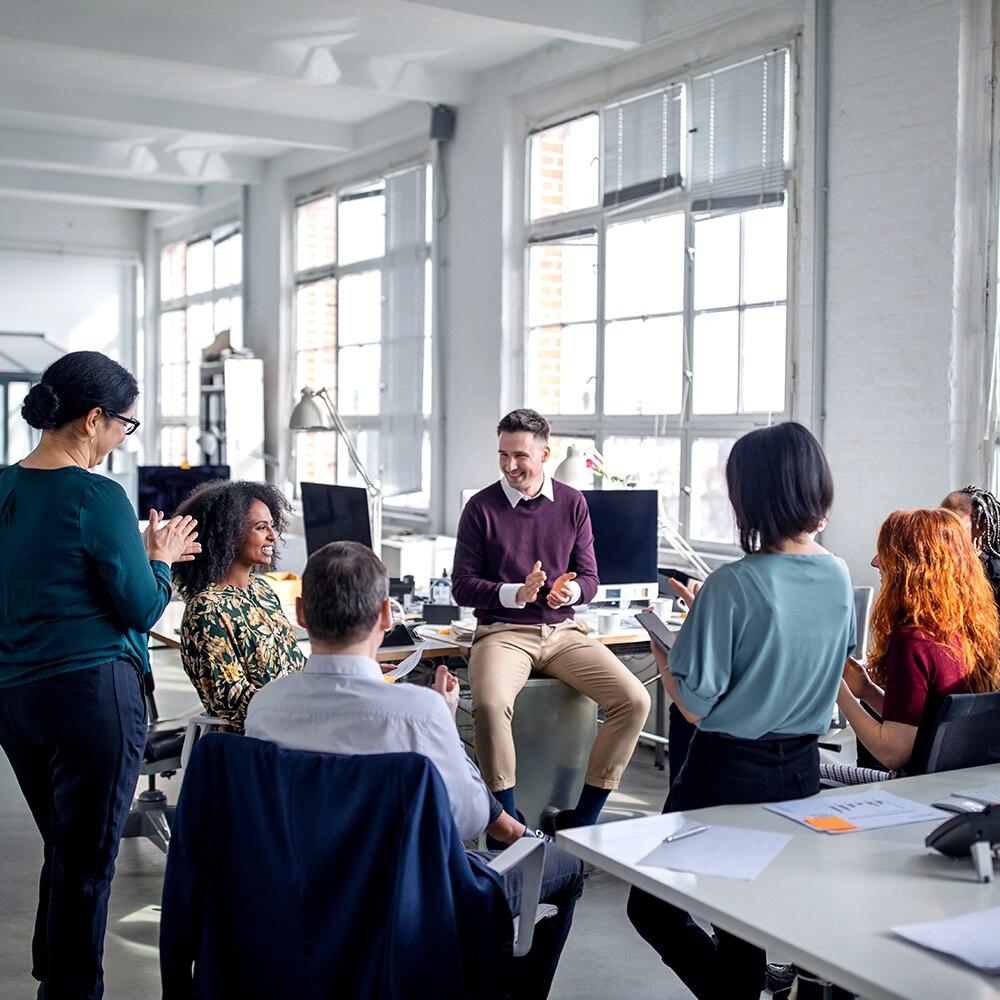Multi-ethnic business team applauding for a female colleague in a meeting.