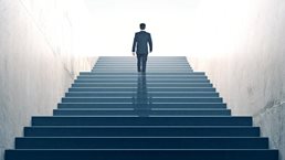 Suited businessperson walking up a multiflight stairway, a few steps from the top