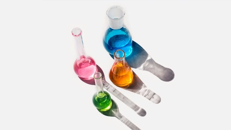 Laboratory glassware containing liquids of different colors on a light gray background. 