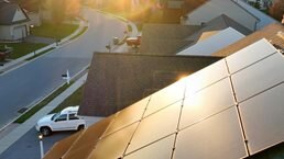 Aerial close up of modern house with solar array reflecting golden hour sunlight.