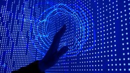 A hand reaching out to touch a deep blue screen covered in datapoint dots. A circular ripple effect emanates from the point of contact.